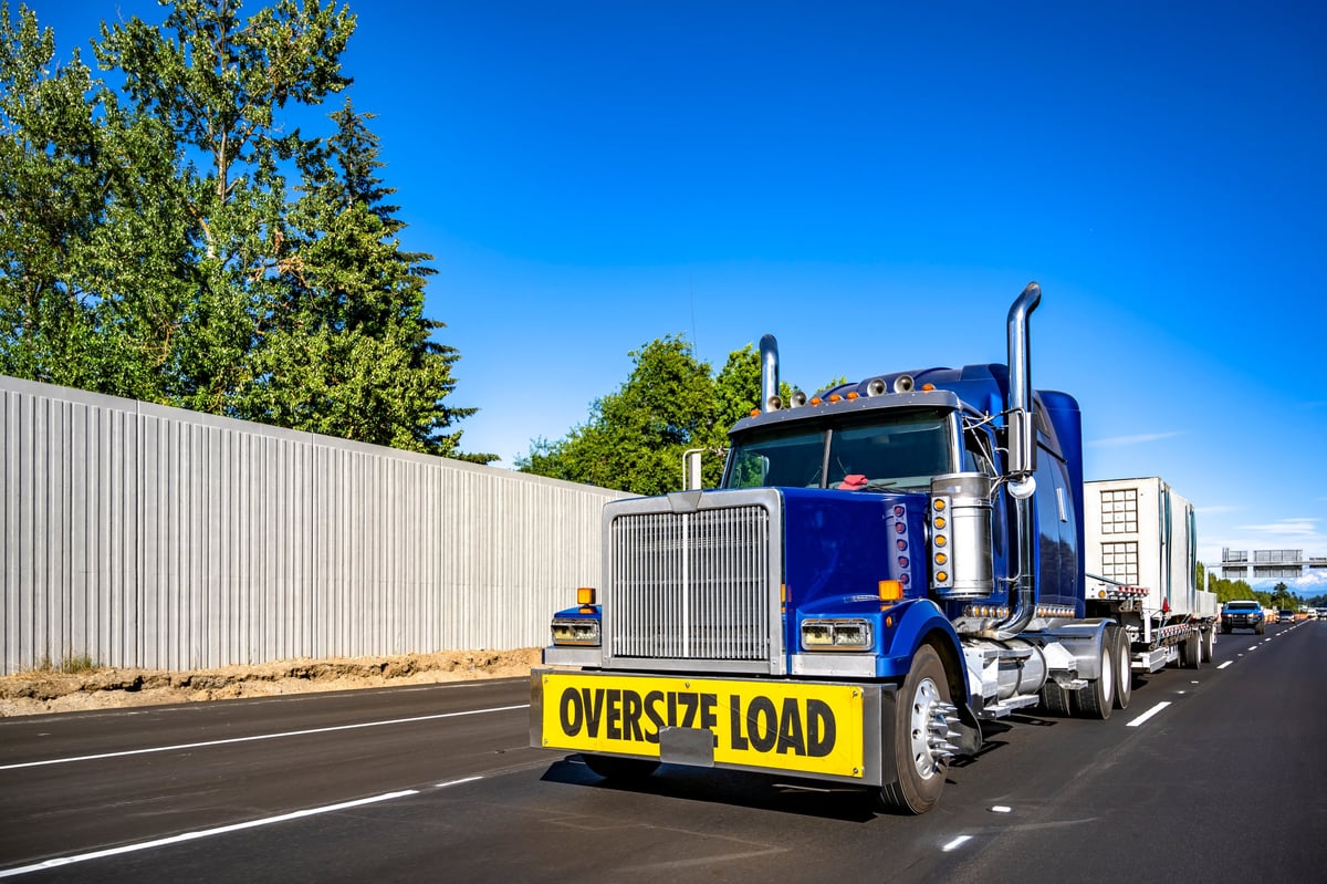 Blue semi truck with oversize load sign carrying oversized cargo on the highway