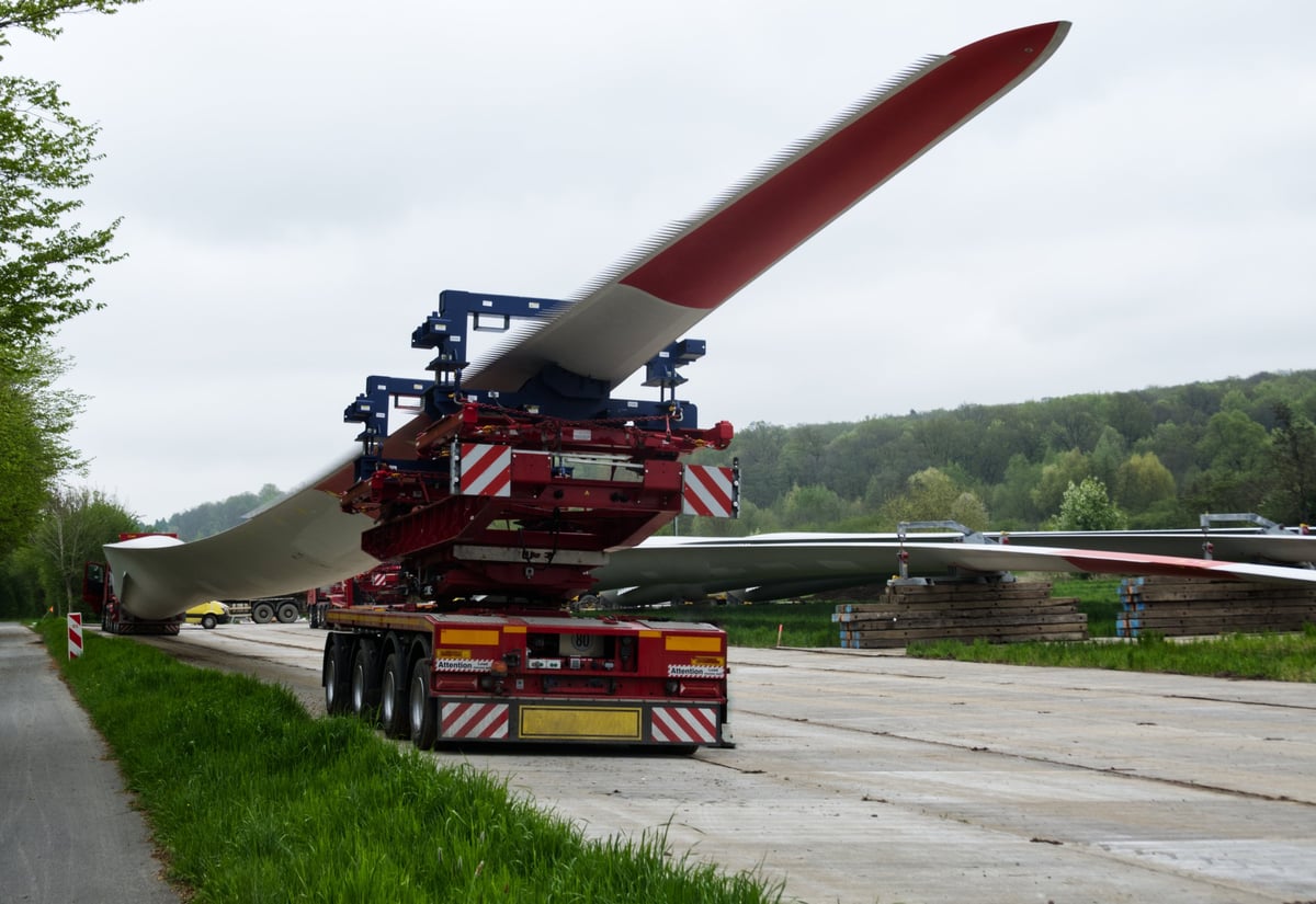 Red and white truck carrying a long wind turbine blade on a specialized trailer
